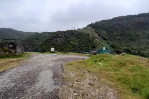 Camino de acceso a la fervenza da roca, con tuberías y vegetación en la ladera.