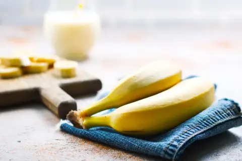 Dwa dojrzałe banany na dżinsowej serwetce, obok pokrojonych bananów i szklanki napoju. Interesuje Cię indeks glikemiczny bananów?