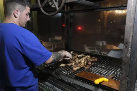 Joven cocinero prepara carnes a la parrilla en un restaurante, quizás en los charros cabo de gata.