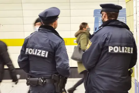 Zwei Polizisten stehen in einer U-Bahn-Station. Im Hintergrund sind 53 Personen zu sehen, die sich bewegen.