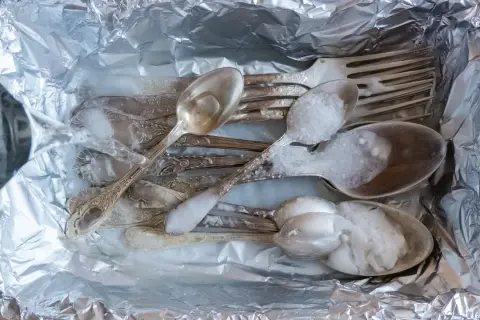 Srebrne sztućce w folii aluminiowej, zalewane wrzątkiem z solą. Prosty sposób, jak wyczyścić srebro w domu.
