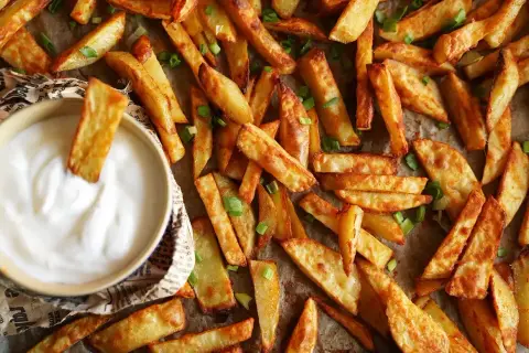 Chrupiące frytki w piekarniku, posypane szczypiorkiem, gotowe do zanurzenia w sosie.