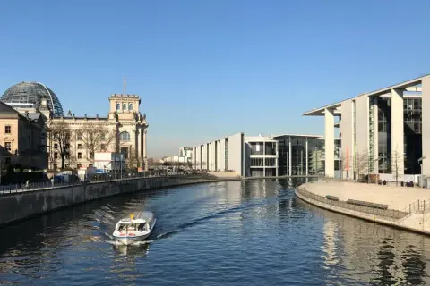 Ein Boot fährt auf der Spree am Reichstagsgebäude und modernen Gebäuden des Regierungsviertels Berlin vorbei.