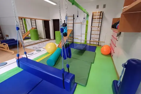 Sala do terapii integracji sensorycznej: huśtawki, drabinki, piłki i materace do ćwiczeń.