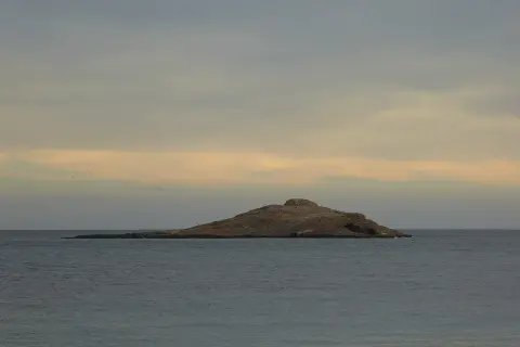 Isla de San Andrés, Almería, un islote rocoso en el mar con gaviotas posadas. Cielo nublado con tonos anaranjados.