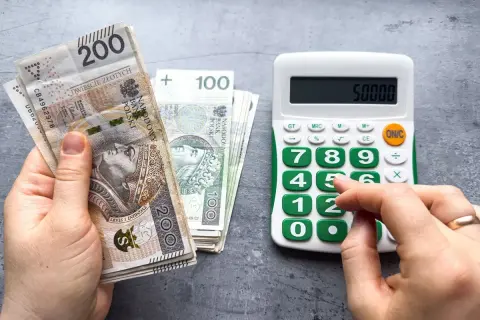 Ręka trzyma banknoty 200 zł i 100 zł, obok kalkulator z wyświetloną kwotą 50000. Czy to już minimalna krajowa?