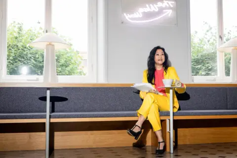 En pr specialist i gul dräkt sitter med papper och kaffe.