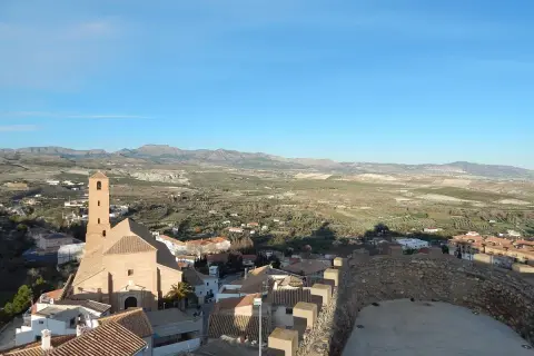 Vistas de Serón que ver: iglesia con campanario, tejados y paisaje rural montañoso bajo un cielo azul.