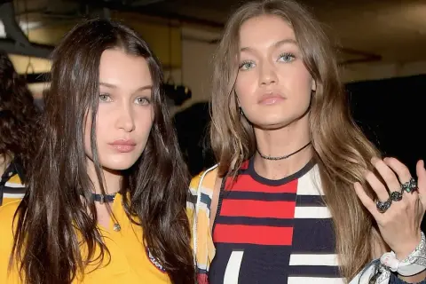 Bella Hadid i Gigi Hadid, siostry i modelki, w modnych stylizacjach. Bella ma ciemne włosy, Gigi jasne. Ich wiek jest nieistotny wobec ich talentu.