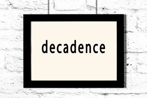 Czarno-biały obraz z napisem "decadence" na jasnym tle, wiszący na białej ceglanej ścianie. To pytanie: co to dekadentyzm?