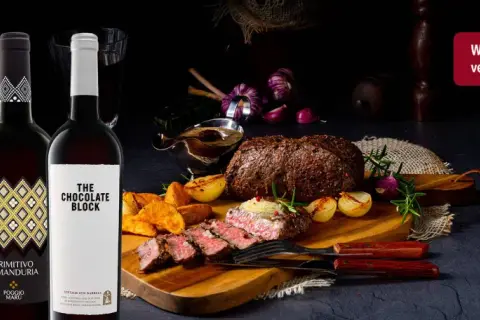 Zwei Flaschen Rotwein neben einem saftigen Wildbraten mit Beilagen. Perfekt, um die Frage zu beantworten: welcher rotwein zum wild kochen.