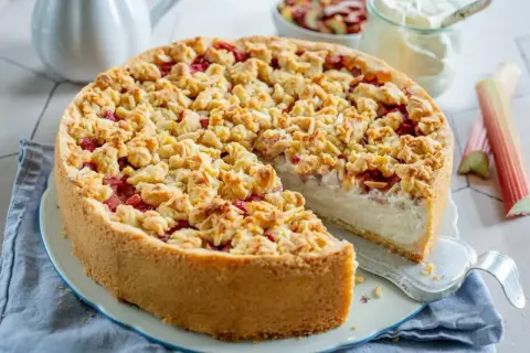 Ein köstlicher Rhabarberkuchen mit Schmand und knuspriger Streuselhaube. Rhabarberstücke sind unter den Streuseln versteckt.