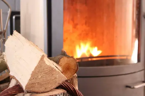 Holzscheite liegen bereit für den Kamin, der gerade nicht benutzt wird. Ein Schornsteinfeger würde sich über die Sauberkeit freuen.