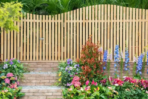 Holz-Gartenzaun-Ideen: Ein schmaler Holzzaun mit Tor, flankiert von bunten Blumen und Ziegelstufen, schafft einen charmanten Eingang.
