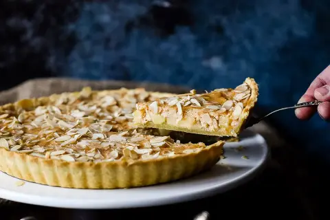 Ein Stück einer sensationellen Apfeltarte mit Mandelblättchen wird herausgehoben. Ein wahrer Genuss!