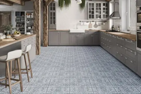 Cocina moderna con suelo hidráulico de diseño geométrico en tonos grises y blancos. Muebles de cocina grises, encimera de madera y barra americana con taburetes.