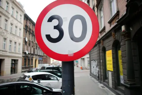Znak ograniczenia prędkości do 30 km/h. Czy skrzyżowanie odwołuje ograniczenie prędkości? Ulica z samochodami i kamienicami.