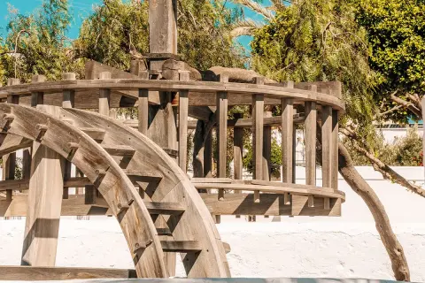 El pozo de los frailes que ver: una noria de madera antigua, rodeada de vegetación exuberante y bajo un cielo azul brillante.