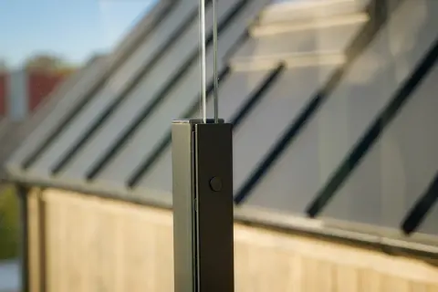 Detaljbild av ett fäste för att montera vindskydd. Glaspanelen är infälld i en svart stolpe.