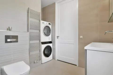 Bagno moderno con doccia e lavatrice vicine. Asciugatrice sopra la lavatrice, vicino a un termosifone cromato e un WC.