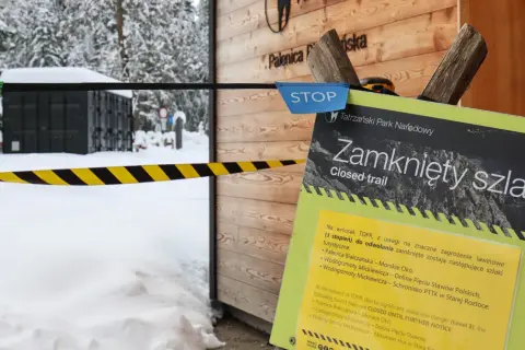 Tablica informacyjna "Zamknięty szlak" w Tatrach zimą, z taśmą ostrzegawczą.