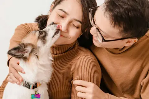 Un tierno momento familiar: un perro lame la nariz de su dueña mientras su pareja lo abraza.