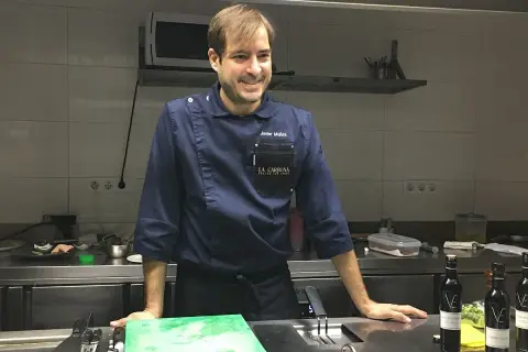 Javier Muñoz chef sonríe en la cocina, con su uniforme azul y el logo de "La Carbona".