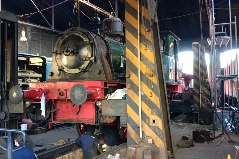 Im Eisenbahnmuseum Dieringhausen stehen mehrere Dampflokomotiven zur Wartung bereit. Eine rote und grüne Lokomotive ist im Vordergrund zu sehen.