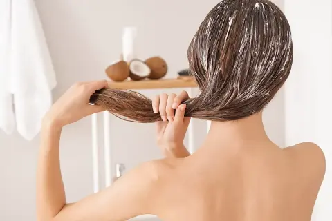Mujer aplicándose mascarilla capilar con aceite de coco. Descubre para qué sirve el aceite de coco para un cabello radiante.