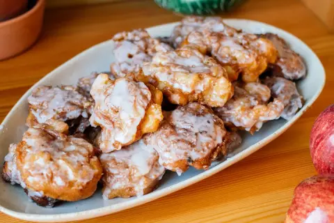 Leckere Apfelkrapfen in der Pfanne, goldbraun gebacken und mit Zuckerguss überzogen, liegen auf einem Teller.