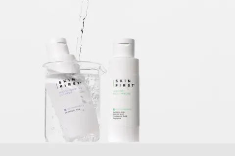 Due flaconi di tonico viso Skin First, uno immerso in un becher con acqua e bollicine, l'altro in piedi.