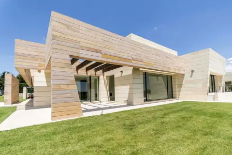 Moderna finca en Madrid con fachada de piedra y madera, césped verde y cielo azul.