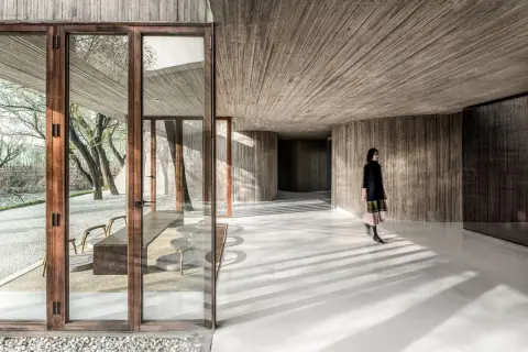 Interior moderno con paredes y techos de hormigón texturizado. Una mujer camina por los suelos de hormigón pulido, proyectando sombras.