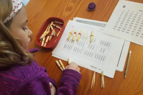 Niña concentrada con pajitas y gomas para resolver operaciones matemáticas, aplicando el método ABN infantil.