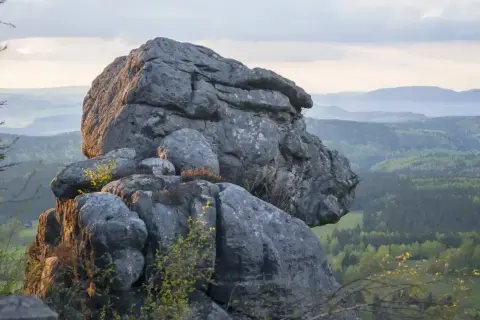 Imponujące, bledne skały górują nad zieloną doliną. Słońce oświetla ich szczyty, tworząc malowniczy krajobraz.