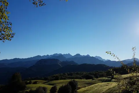 Paisaje montañoso con un bosque peloño al amanecer. El sol ilumina las cumbres y el cielo azul se extiende sobre la naturaleza.