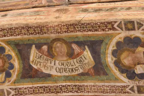 Angeli con pergamena negli affreschi dell'abbazia di Pomposa. Dettaglio di un volto angelico con ali e iscrizione latina, parte di un ciclo pittorico antico.