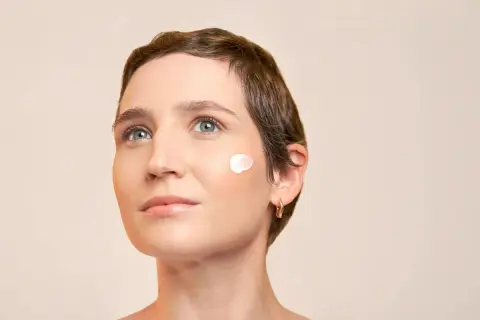 Une femme au regard pensif, avec une touche de crème solaire avant ou après crème hydratante sur la joue.