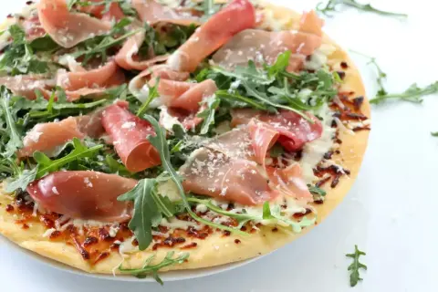 Pyszna pizza prosciutto z rukolą i parmezanem, idealna na letni wieczór.