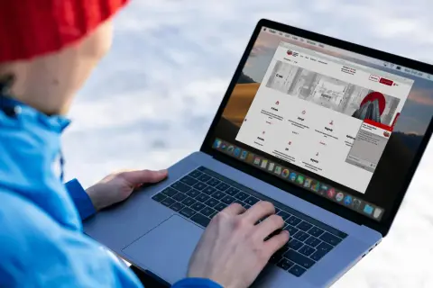 Osoba w czerwonej czapce i niebieskiej kurtce korzysta z laptopa, na ekranie którego widoczna jest strona internetowa KRD.