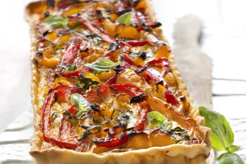 Tarte rectangulaire aux poivrons rouges et jaunes grillés, garnie de basilic frais. Un délice coloré et savoureux.