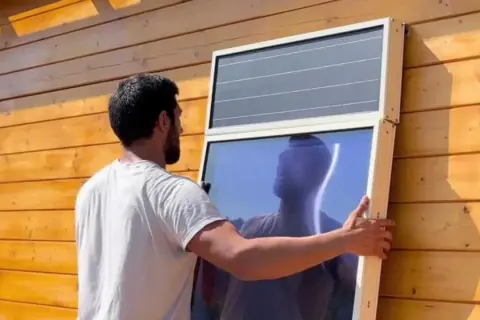 Hombre instala panel solar para calefacción en pared de madera.