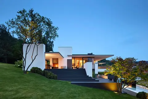 Moderne Villa mit breiter, dunkler Treppe zum Hauseingang. Tolle Ideen für Haus und Treppe, beleuchtet bei Dämmerung.