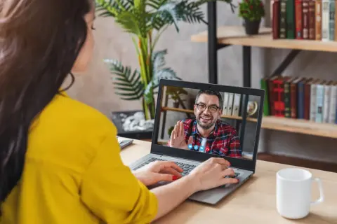 Kobieta na wideo rozmowie z mężczyzną, który uśmiecha się i macha. Może to być konsultacja online, np. test na aspergera.