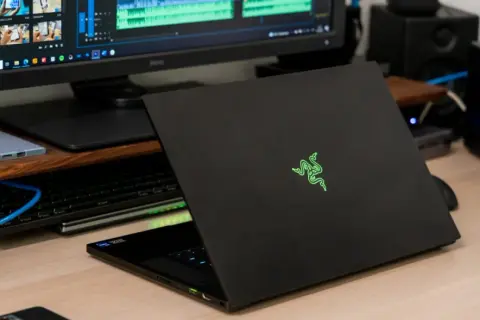 Czarny laptop Razer z podświetlanym logo, obok monitor z edytorem wideo i dysk sieciowy. Prawdopodobnie najdroższy komputer gamingowy na świecie.