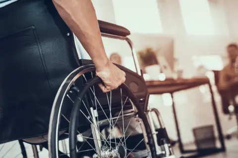 Dłoń na kółku wózka inwalidzkiego. Zastanawiasz się, jaka emerytura po świadczeniu pielęgnacyjnym?