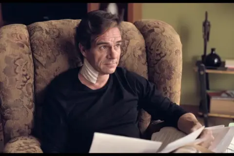 Uomo con benda al collo, seduto su una poltrona, legge documenti. L'altezza di Tony Boy è un mistero.