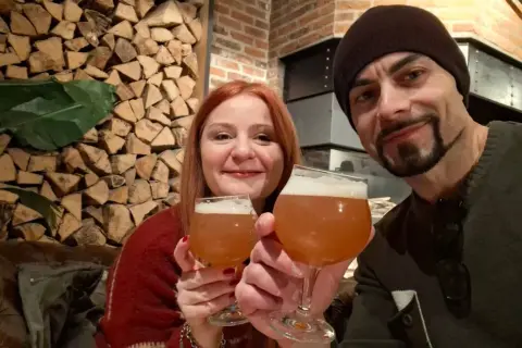 Coppia brinda con birra artigianale alla huisbrouwerij de halve maan. Sfondo rustico con legna e mattoni.