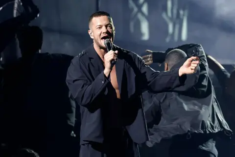 Imagine Dragons koncert Polska: wokalista Dan Reynolds śpiewa na scenie, otoczony tancerzami w mrocznym klimacie.