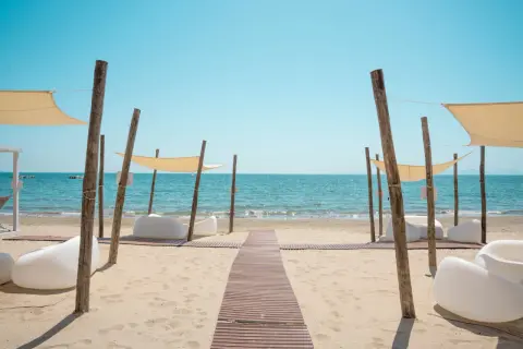 Un percorso in legno conduce al mare cristallino del golfo di Follonica, tra comode sedute bianche e tende parasole.